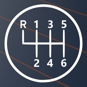 May include: White graphic of a six-speed manual transmission gear shift pattern, including reverse (R), on a dark blue background. The numbers 1 to 6 are clearly displayed within a circular outline.