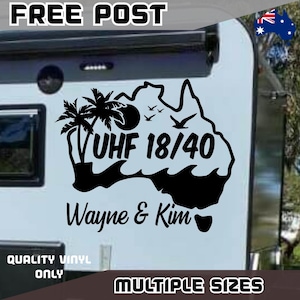 May include: A black vinyl decal applied to a white surface, featuring the outline of Australia, palm trees, a sun, birds, and waves. The text reads UHF 18/40 and Wayne & Kim. The design includes a small Australian flag icon in the top right corner.