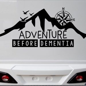 May include: Black graphic of a mountain range with three birds and a compass rose. The text reads "ADVENTURE BEFORE DEMENTIA" in a bold, sans-serif font. Ideal for outdoor enthusiasts and travel lovers.