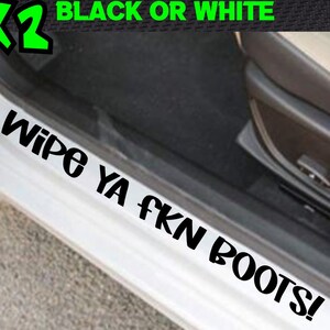 May include: Black or white car door sill sticker with the text "WIPE YA FKN BOOTS!". The sticker is shown on a white car door frame. The image also includes a green "x2" graphic.