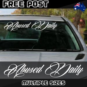 May include: White vinyl car sticker with the words "Abused Daily" in a cursive font, shown on a car windscreen. The image also includes the text "FREE POST" and "MULTIPLE SIZES".