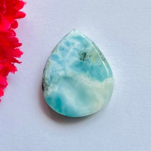 May include: A teardrop-shaped cabochon of blue and white ocean jasper with a swirling pattern. The stone has a smooth, polished surface.