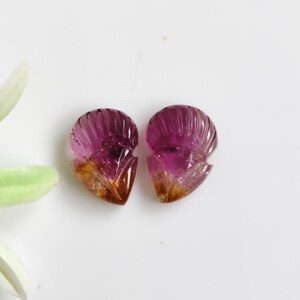 May include: Two carved gemstone pieces featuring a fan-like shape with vertical grooves. The stones exhibit a gradient colour transition from a deep magenta pink at the top to a warm amber brown at the pointed base, with a translucent finish.