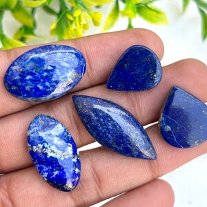 Peut inclure: Cinq cabochons en lapis-lazuli bleu et blanc avec des paillettes dorées. Les cabochons sont de formes et de tailles variées, notamment ovales, en forme de larme et en forme de poire.