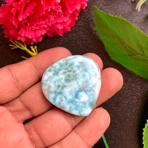 Puede incluir: Un cabujón de jaspe oceánico en forma de corazón de color azul claro y blanco con un patrón único de inclusiones blancas y marrones.