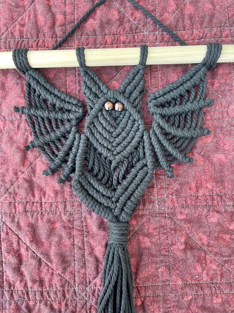 May include: Black macrame bat wall hanging with wooden dowel and brown wooden bead eyes.