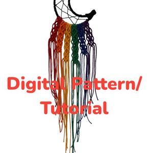 Op de afbeelding: Een handgemaakte macramé dromenvanger in de vorm van een halve maan. De bovenkant is zwart, met een webontwerp in de maan. Daaronder hangen regenboogkleurige macramé strengen. De tekst "Digital Pattern/Tutorial" is rood.