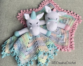 May include: A crocheted baby blanket with a pastel rainbow pattern and a crocheted unicorn attached. The blanket has a pink crocheted border with a scalloped edge. The blanket is made with a soft yarn and is perfect for a baby shower gift.