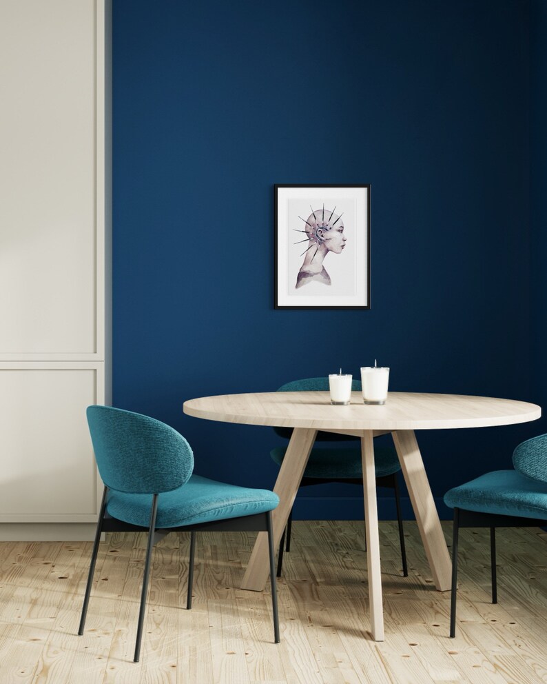 May include: A round wooden table with a blue and white watercolor print of a woman with a spiky hairdo hanging on the wall behind it. Two teal chairs are placed on either side of the table.
