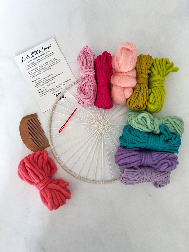 May include: A craft kit for making a wall hanging with colorful yarn. The kit includes a wooden hoop, a comb, a needle, and 10 skeins of yarn in various colors, including pink, green, purple, and blue. The kit is labeled "Lush Little Loops Candy Rainbow Weaving Kit".
