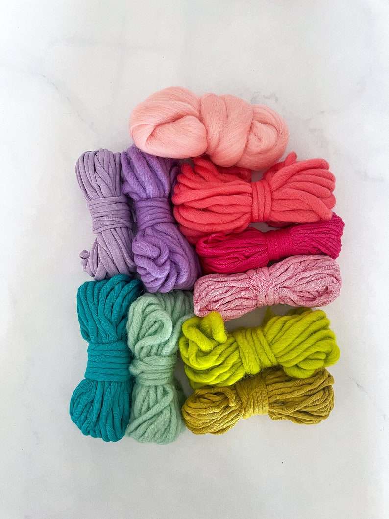 May include: A set of eight colorful yarn skeins in various shades of pink, purple, teal, green, and yellow. The yarn is arranged in a stack, with the pink skein on top.