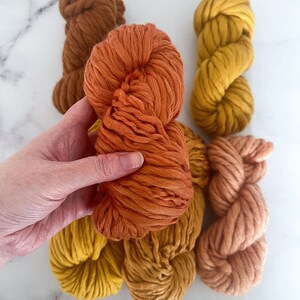 May include: Five balls of yarn in various shades of orange, yellow, and brown. The yarn is thick and fluffy, perfect for knitting or crocheting.