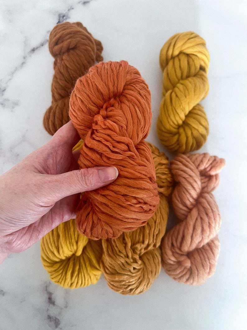 May include: Five balls of yarn in various shades of orange, yellow, and brown. The yarn is thick and fluffy, perfect for knitting or crocheting.