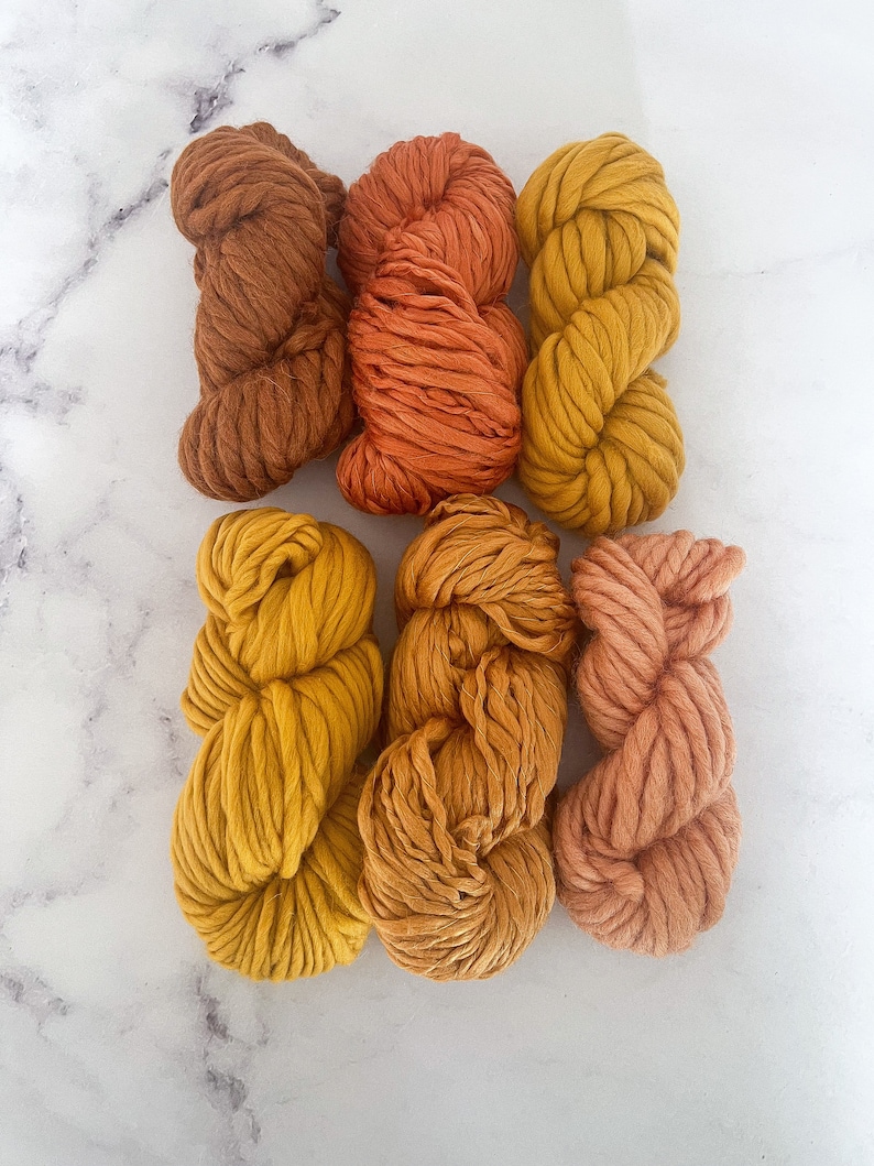 May include: Six skeins of yarn in various shades of orange, yellow, and brown. The yarn is arranged in a row, with the darkest shade on the left and the lightest shade on the right.