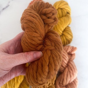 May include: Three skeins of yarn in shades of orange, yellow, and brown. The yarn is thick and fluffy, perfect for knitting or crocheting.
