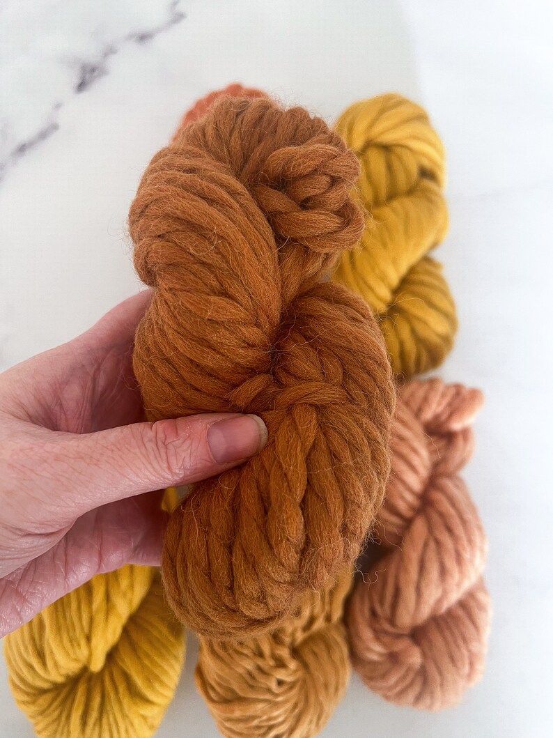 May include: Three skeins of yarn in shades of orange, yellow, and brown. The yarn is thick and fluffy, perfect for knitting or crocheting.