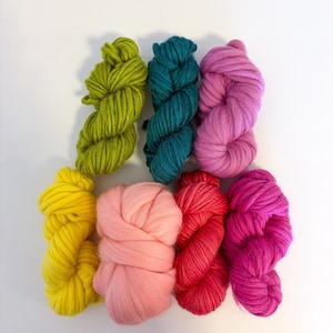 May include: Seven skeins of colorful, chunky yarn in shades of yellow, green, teal, pink, and red. The yarn is arranged in a visually appealing pattern, perfect for knitting or other fiber art projects. The texture of the yarn is thick and inviting.