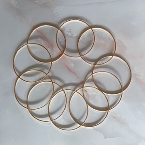 May include: A set of ten gold-toned bangle bracelets arranged in a circular pattern on a white marble surface.