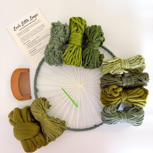 May include: A Lush Little Loops weaving kit with various shades of green yarn, a wooden comb, a weaving needle, and a circular loom. The kit includes a printed instruction sheet. The yarn colors range from light to dark green.