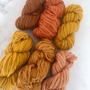 May include: Assortment of yarn in shades of orange, yellow, and brown. The yarn is thick and fluffy, perfect for knitting or crocheting.