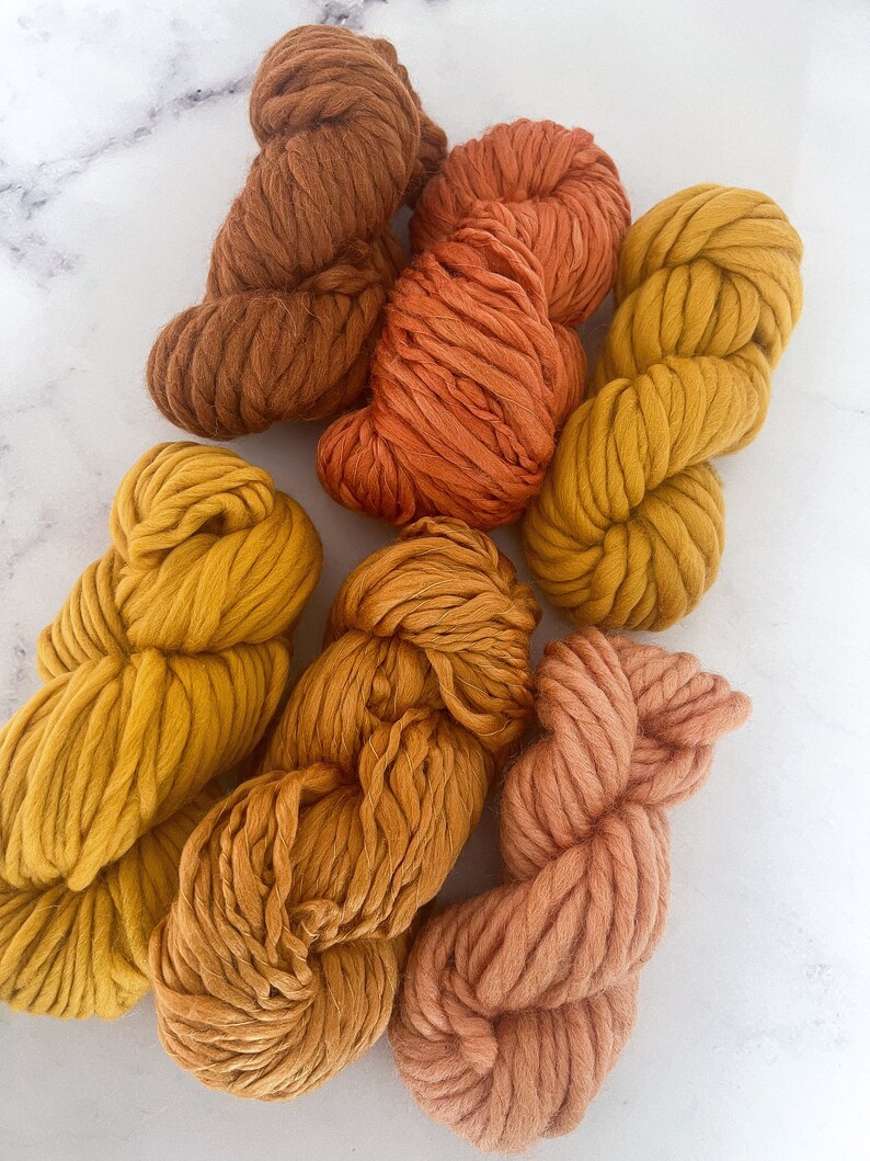 May include: Assortment of yarn in shades of orange, yellow, and brown. The yarn is thick and fluffy, perfect for knitting or crocheting.