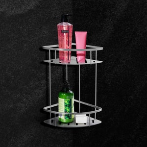 Może przedstawiać: Dwupiętrowa narożna półka prysznicowa wykonana ze srebrnego metalu. Półka ma różową butelkę żelu pod prysznic i różową tubkę balsamu na górnej półce. Dolna półka ma zieloną butelkę żelu pod prysznic i biały kawałek mydła.