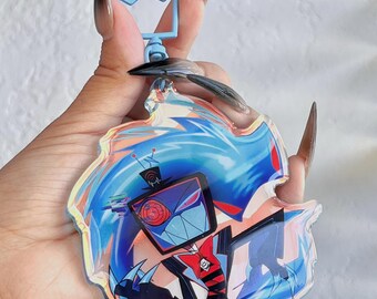 May include: A clear acrylic keychain featuring a cartoon character with a square head, red bow tie, and black suit. The design is set against a blue and orange background with a blue crown-shaped clasp.