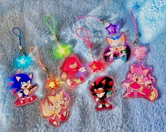 May include: A set of eight colourful character charms with attached strings and star-shaped charms. The characters include Sonic the Hedgehog, Tails, Knuckles, Shadow, Amy Rose, Rouge the Bat, and Cream the Rabbit.