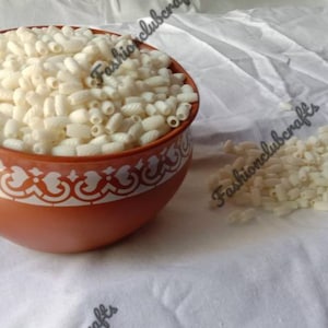 Pode incluir: Uma tigela de terracota cheia de arroz tufado branco, com mais arroz tufado espalhado sobre uma superfície de tecido branco.
