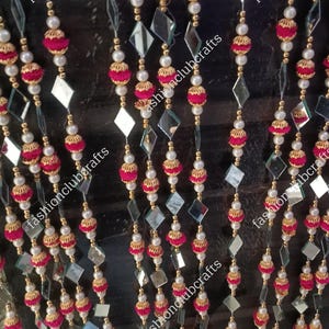 May include: Decorative beaded curtain with alternating strands of red fabric balls, white pearls, and diamond-shaped mirrors. Gold-colored accents and bell-shaped charms at the bottom. The text "fashionclubcrafts" is visible on the image.