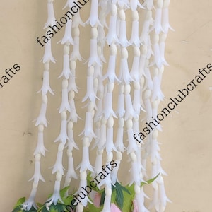 May include: A string of white plastic flowers with pink rose buds at the bottom. The flowers are arranged in a cascading pattern and the text "fashionclubcrafts" is repeated throughout the image.