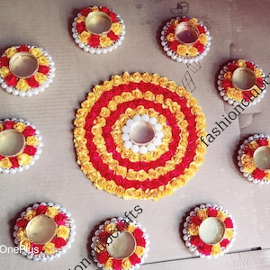 Könnte beinhalten: Ein Set aus neun dekorativen Kerzenhaltern aus roten und gelben Stoffblumen. Die Kerzenhalter sind in einem Kreis angeordnet, mit einem größeren, runden Mittelstück in der Mitte. Das Mittelstück besteht ebenfalls aus roten und gelben Stoffblumen.