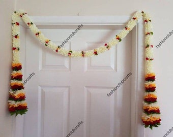 May include: A white floral garland with red, orange, and yellow accents hangs on a white door. The garland is made of artificial flowers and is a traditional Indian decoration.
