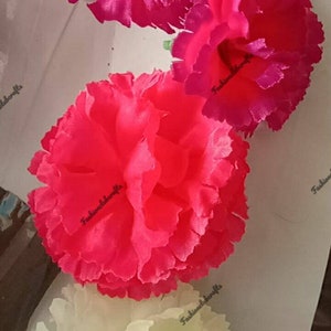 May include: Three artificial flowers in different colors: pink, red, and white. The flowers are made of fabric and have a ruffled texture. The flowers are arranged in a vertical stack, with the pink flower on top, the red flower in the middle, and the white flower on the bottom.