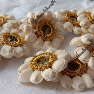 K&ouml;nnte beinhalten: Ein Set mit 8 wei&szlig;en Stoffblumen-Verzierungen mit goldenen Verzierungen. Jede Blume hat einen Mittelkreis mit goldener Umrandung und einem gr&uuml;nen Zentrum.