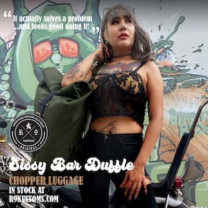 Op de afbeelding: Een olijfgroene duffeltas met zwarte banden, met het opschrift "Sissy Bar Duffle" en "Chopper Luggage". De tas maakt deel uit van de collectie "Hand Made Motorcycle Gear". De afbeelding bevat de tekst "It actually solves a problem...and looks good doing it!"