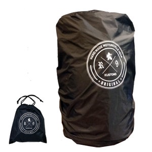 Könnte beinhalten: Schwarzer Regenschutz für einen Motorrad-Rucksack mit einem weißen Logo, auf dem "Hand Made Motorcycle Gear R9 Kustoms Original" steht. Eine kleinere schwarze Kordeltasche mit dem gleichen Logo ist ebenfalls abgebildet.