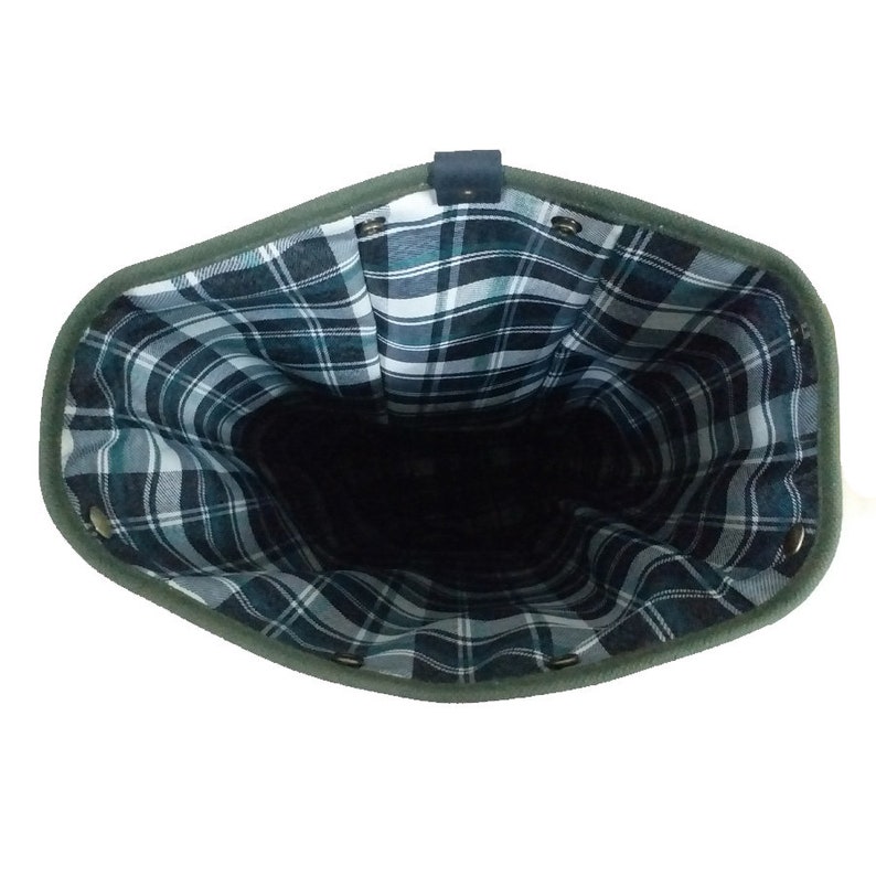 Op de afbeelding: Een open, olijfgroene tas met een donker geruit interieur. De tas heeft een donker leren riem en metalen ogen rond de bovenkant. Het ruitpatroon heeft tinten blauw, groen en wit.