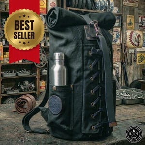 May include: A dark green canvas roll-top backpack featuring a side pocket containing a silver metal water bottle. The bag has a vertical lace-up design with dark leather straps and a circular leather patch on the front pocket.