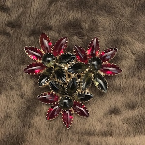May include: A gold tone brooch with red and green glass stones in a floral design.