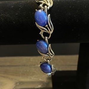 May include: A silver bracelet with blue oval-shaped stones set in a floral design.