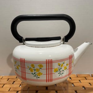 May include: White enamel teapot with a black handle and lid. The teapot has a red and white checkered pattern with yellow flowers.