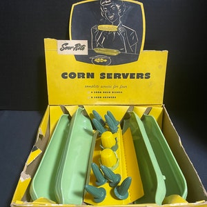 May include: A yellow box with a green and yellow corn on the cob design. The box contains a set of four green corn husk dishes and eight yellow and green corn skewer holders. The box reads "Serv-Rite Corn Servers complete service for four 4 Corn Husk Dishes 8 Corn Skewers Colors: Green".