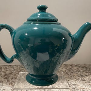 May include: A teal blue ceramic teapot with a rounded body and a lid. The teapot has a spout and a handle.