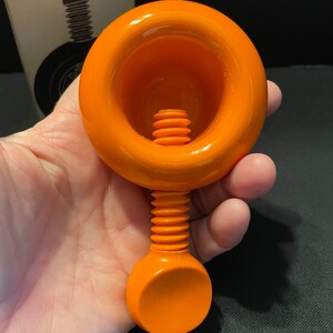 May include: Orange plastic nutcracker with a screw mechanism. The nutcracker has a round top with a deep well and a round handle.
