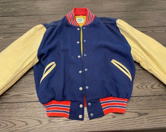 May include: A blue and cream varsity jacket with red and white stripes on the collar and cuffs. The jacket has a snap closure and two pockets.