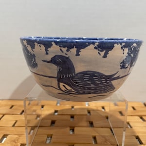 May include: A white ceramic bowl with a blue and white design of a bird. The bowl is on a wooden surface.