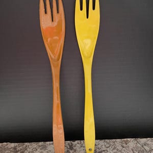 May include: Two plastic serving forks, one brown and one yellow. The forks have a unique design with a wide, flat handle and three tines.