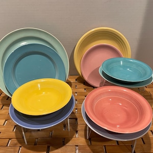 May include: A set of six colorful ceramic bowls and plates in shades of blue, yellow, pink, and green. The bowls and plates are stacked on top of each other and are arranged in a circular pattern.