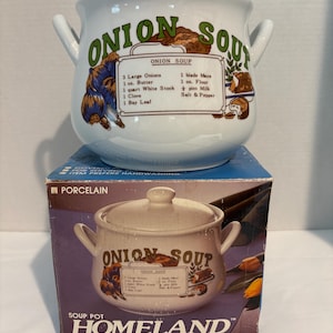 May include: A white porcelain onion soup pot with a lid and two side handles. The front features green text reading ONION SOUP and a printed recipe listing ingredients like 3 Large Onions, 1 oz. Butter, and 1 quart White Stock. It sits on its box.